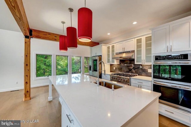 kitchen featuring decorative light fixtures, white cabinetry, sink, stainless steel appliances, and a center island with sink