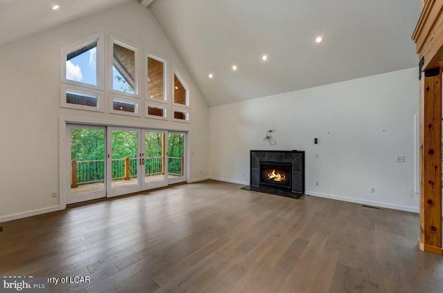 unfurnished living room with a tiled fireplace, wood-type flooring, high vaulted ceiling, and french doors