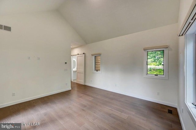 empty room with hardwood / wood-style flooring, a barn door, and vaulted ceiling