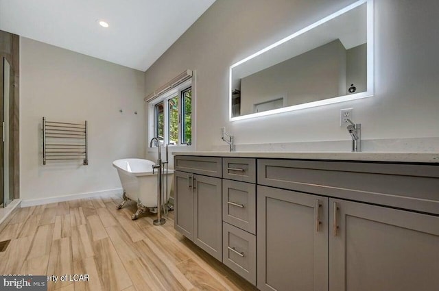 bathroom with vaulted ceiling, wood-type flooring, a bathtub, and vanity