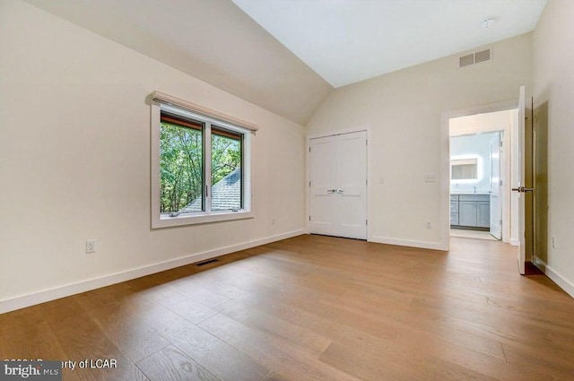 unfurnished bedroom with vaulted ceiling, ensuite bathroom, and light wood-type flooring