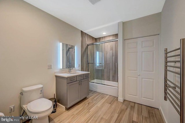 full bathroom with combined bath / shower with glass door, radiator heating unit, hardwood / wood-style flooring, vanity, and toilet