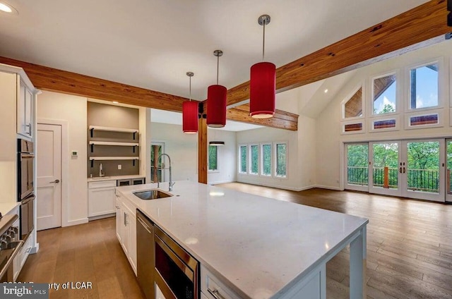 kitchen with hanging light fixtures, an island with sink, sink, and white cabinets