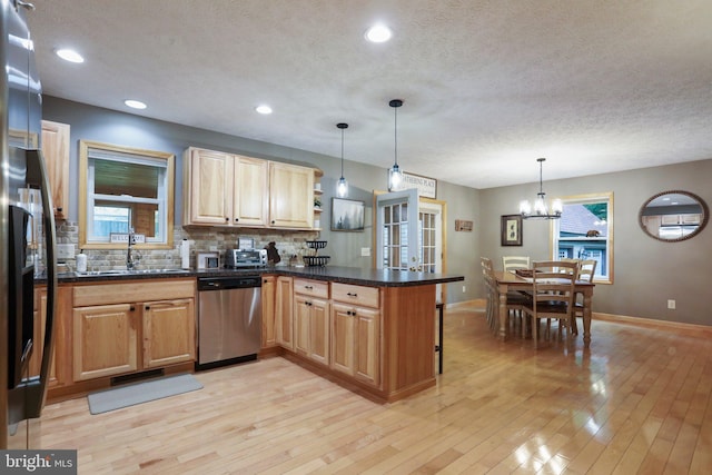 kitchen featuring sink, hanging light fixtures, light wood-type flooring, stainless steel dishwasher, and kitchen peninsula