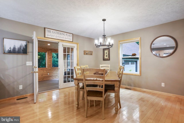 dining space featuring a notable chandelier, a textured ceiling, light hardwood / wood-style floors, and french doors