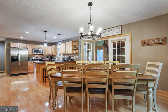 dining space featuring ceiling fan with notable chandelier, sink, a textured ceiling, and light wood-type flooring