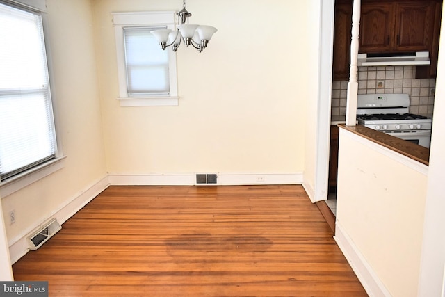 unfurnished dining area with plenty of natural light, an inviting chandelier, and light hardwood / wood-style floors