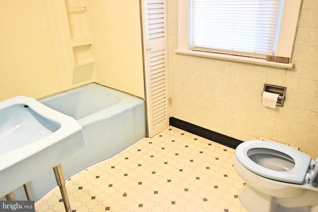 bathroom featuring tile walls, a tub to relax in, and toilet