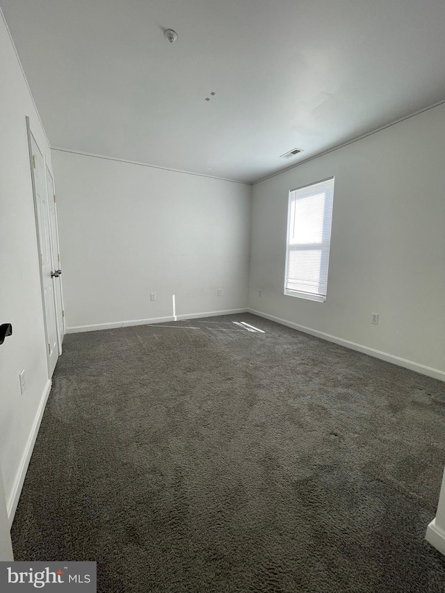 empty room featuring visible vents, dark carpet, and baseboards