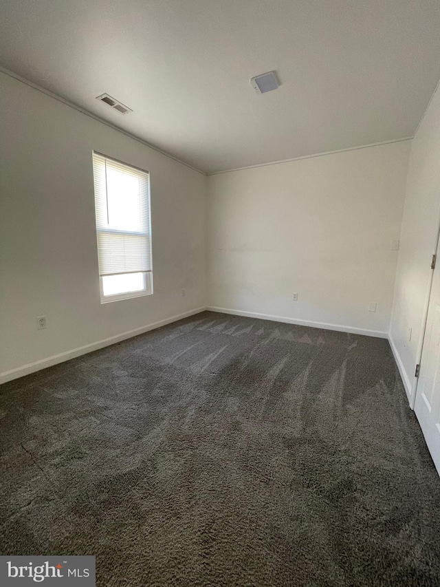 spare room featuring dark colored carpet, visible vents, and baseboards