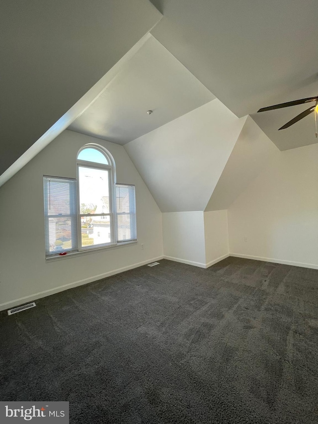 additional living space with vaulted ceiling, baseboards, visible vents, and dark colored carpet