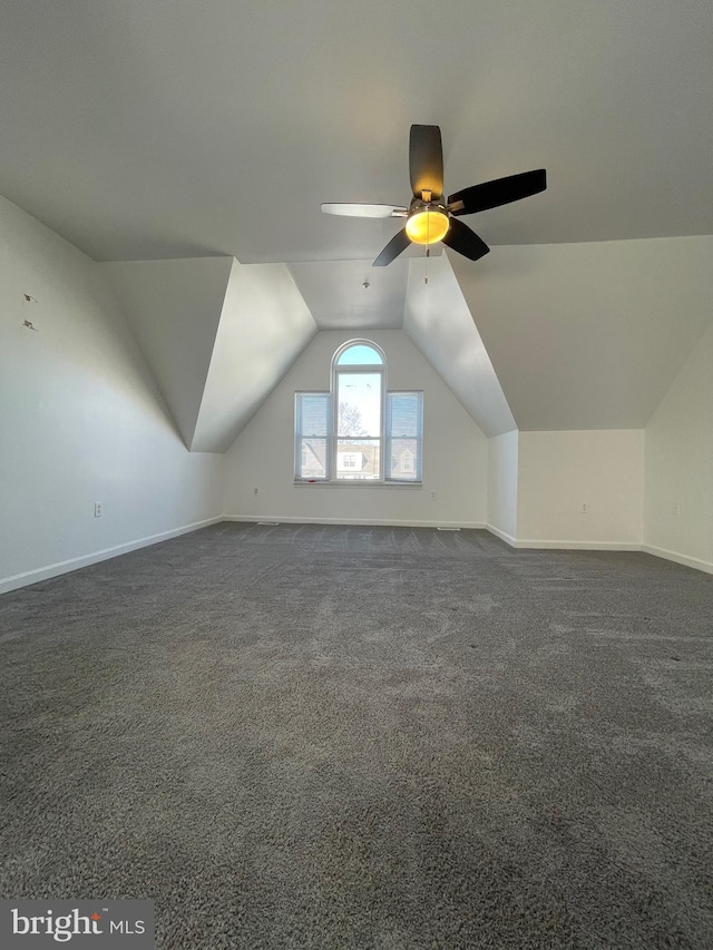 additional living space with baseboards, a ceiling fan, dark colored carpet, and vaulted ceiling