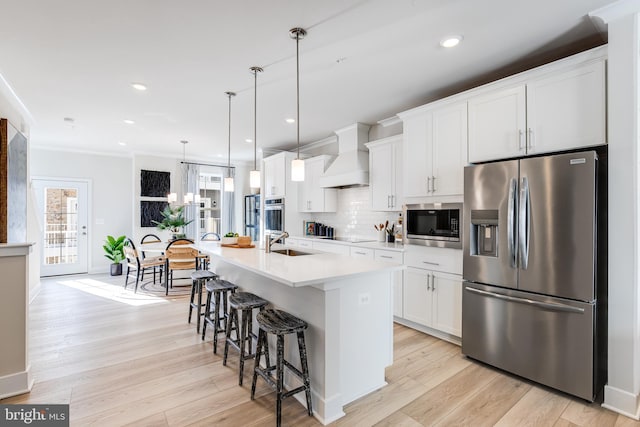 kitchen with premium range hood, appliances with stainless steel finishes, pendant lighting, white cabinets, and a kitchen island with sink