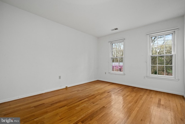 empty room with light wood-style floors, baseboards, and visible vents