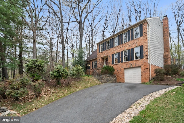 view of front of house with brick siding, a chimney, an attached garage, and aphalt driveway