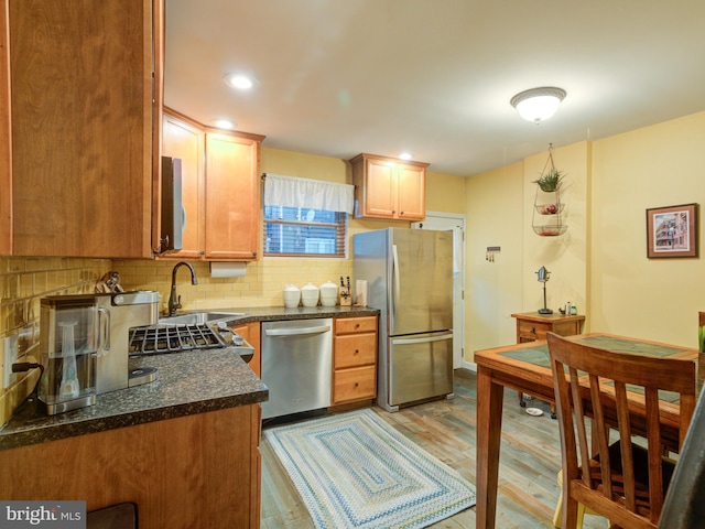 kitchen with appliances with stainless steel finishes, sink, backsplash, and light hardwood / wood-style flooring