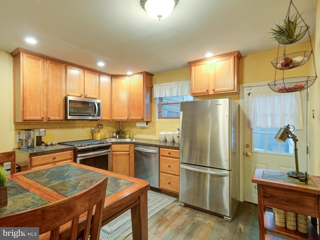 kitchen with stainless steel appliances, tasteful backsplash, dark stone countertops, and light hardwood / wood-style floors