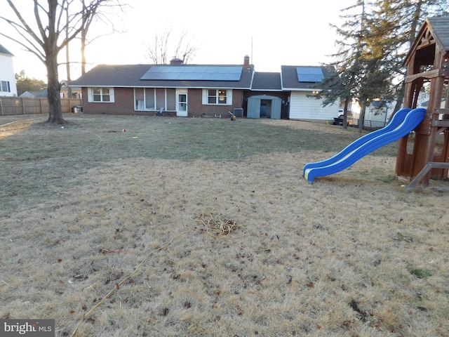 rear view of house with a playground, a yard, and solar panels