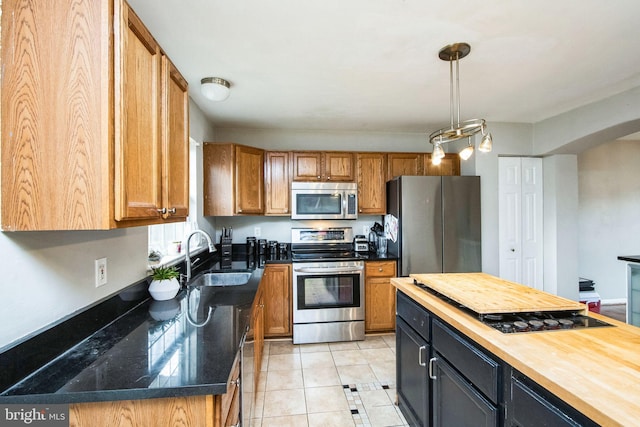 kitchen with butcher block countertops, sink, decorative light fixtures, light tile patterned floors, and stainless steel appliances