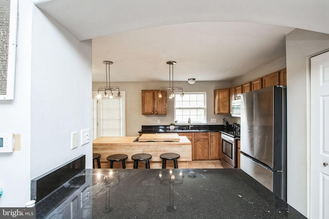 kitchen with stainless steel appliances, sink, dark stone countertops, and decorative light fixtures