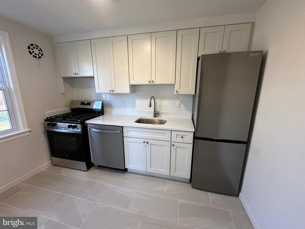 kitchen with sink, stainless steel appliances, white cabinets, light tile patterned flooring, and decorative backsplash