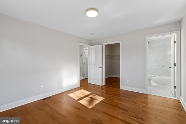 unfurnished bedroom with hardwood / wood-style flooring, a walk in closet, ensuite bath, and a closet