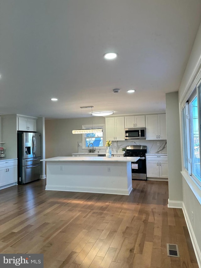 kitchen with a center island, hanging light fixtures, dark hardwood / wood-style flooring, stainless steel appliances, and white cabinets