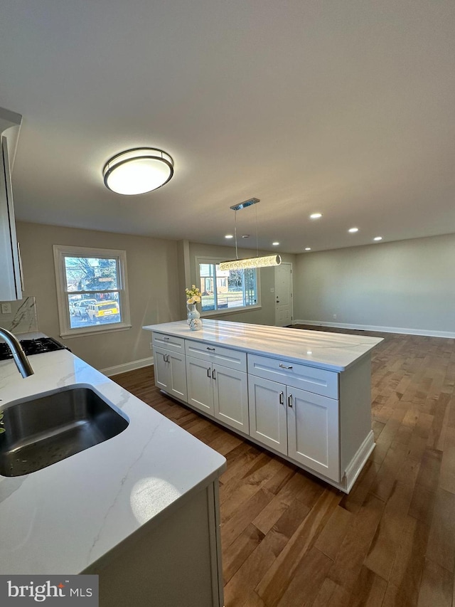 kitchen featuring sink, white cabinetry, hanging light fixtures, light stone counters, and a kitchen island