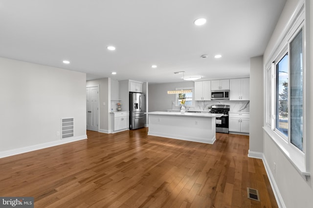 kitchen featuring appliances with stainless steel finishes, white cabinetry, backsplash, a center island with sink, and dark hardwood / wood-style flooring