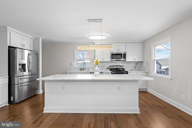 kitchen with pendant lighting, appliances with stainless steel finishes, a wealth of natural light, white cabinets, and a kitchen island