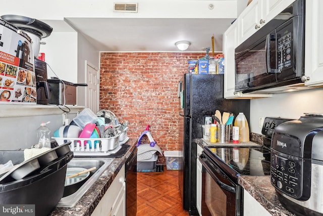 kitchen featuring dark parquet floors, black appliances, white cabinets, brick wall, and dark stone counters