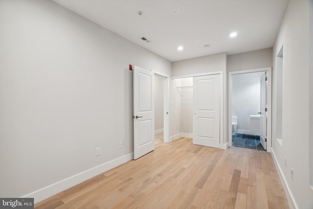 unfurnished bedroom with a closet, ensuite bath, and light hardwood / wood-style flooring