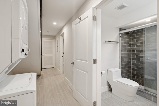 bathroom featuring toilet, stacked washing maching and dryer, and a shower with door