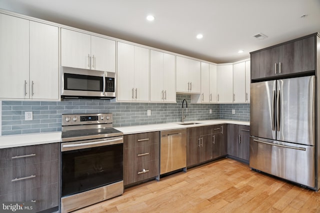 kitchen with dark brown cabinetry, sink, white cabinetry, stainless steel appliances, and light hardwood / wood-style floors