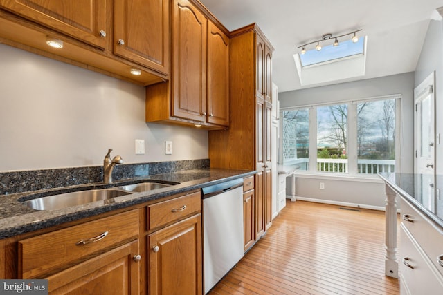 kitchen featuring a skylight, a sink, stainless steel dishwasher, light wood finished floors, and brown cabinetry