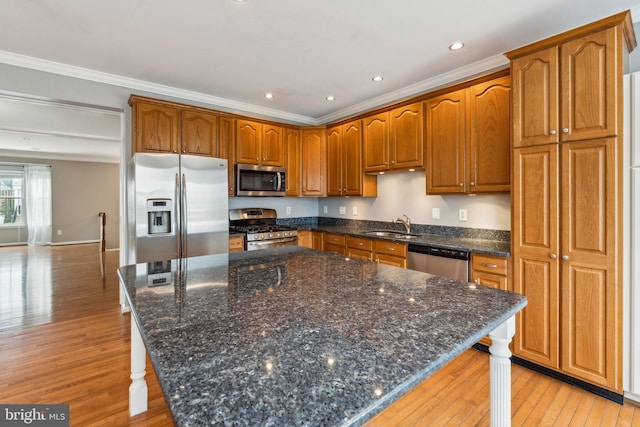 kitchen with crown molding, light wood finished floors, stainless steel appliances, a sink, and a kitchen island