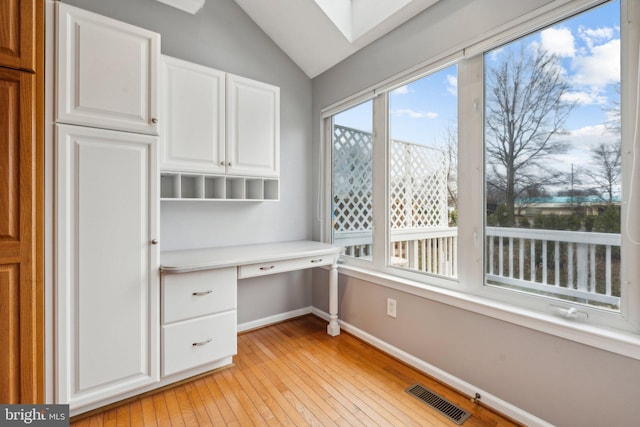 unfurnished office with vaulted ceiling with skylight, light wood-style flooring, visible vents, baseboards, and built in desk