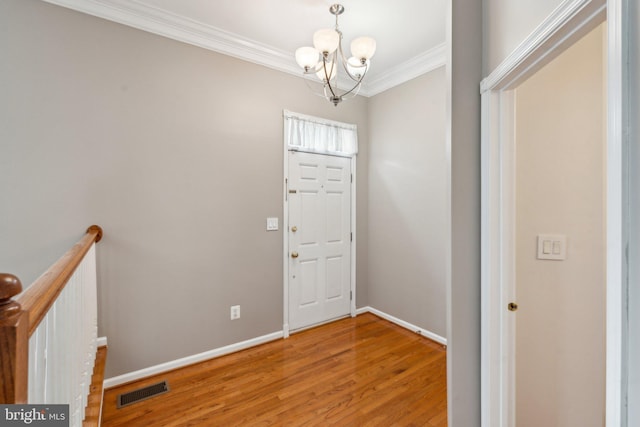 entryway featuring crown molding, a notable chandelier, visible vents, wood finished floors, and baseboards