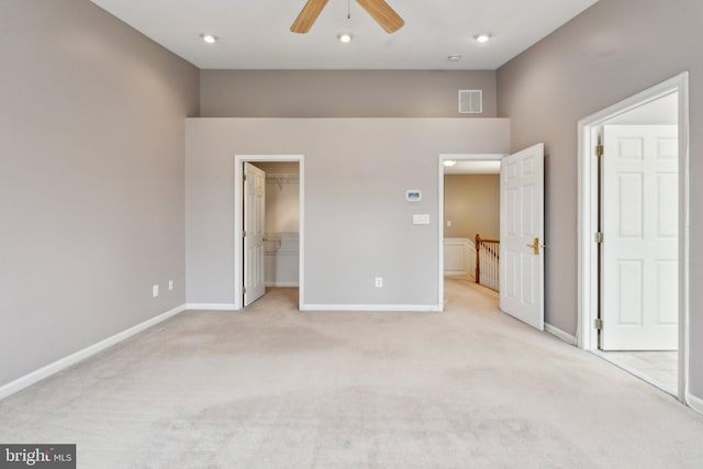 unfurnished bedroom with baseboards, visible vents, light colored carpet, a walk in closet, and a closet