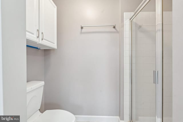 bathroom with toilet, a shower stall, and baseboards