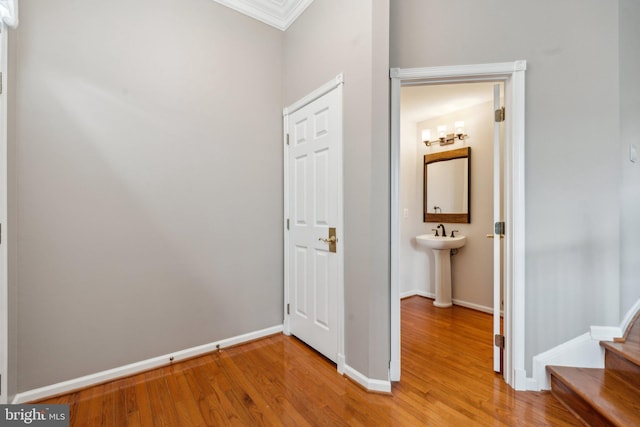 hallway featuring baseboards, crown molding, and light wood-style floors