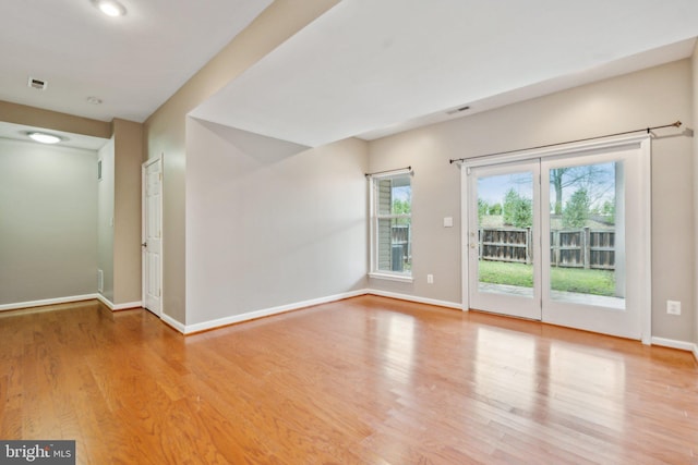 spare room with wood finished floors, visible vents, and baseboards