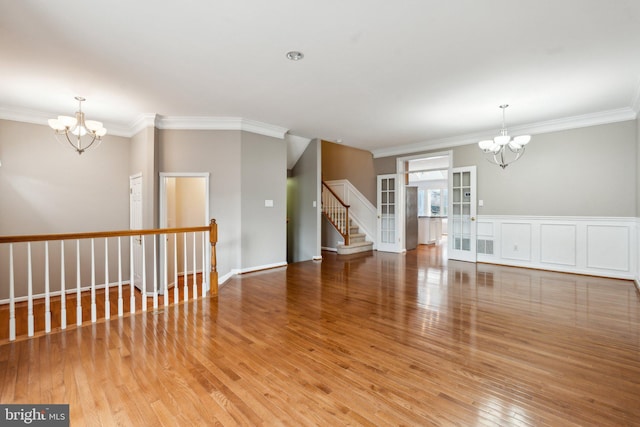 empty room with hardwood / wood-style floors, crown molding, stairway, and a notable chandelier