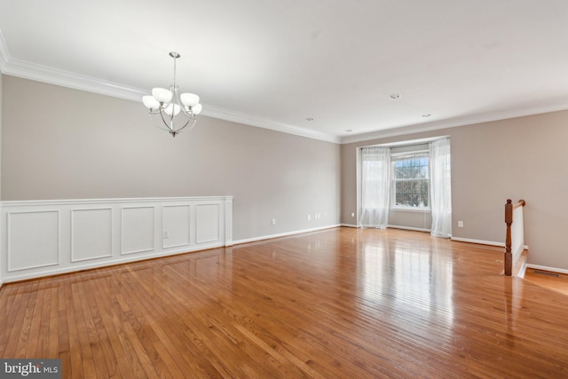 unfurnished room with a chandelier, baseboards, hardwood / wood-style flooring, and crown molding