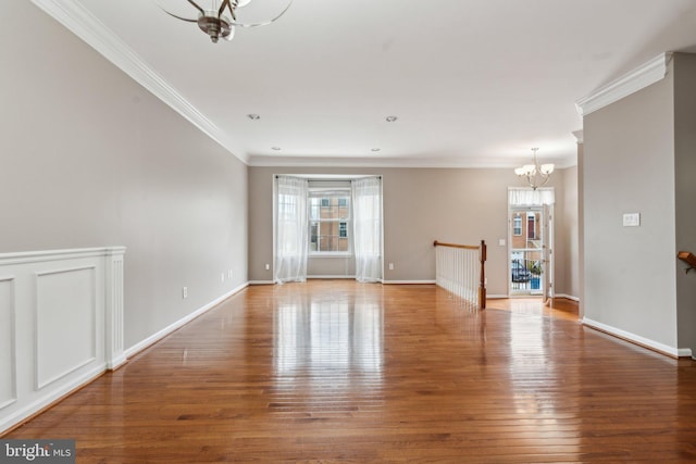 unfurnished room featuring wood finished floors, crown molding, baseboards, and an inviting chandelier