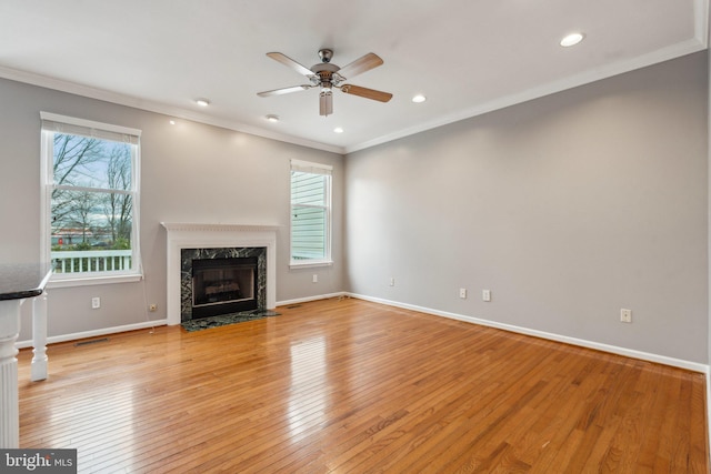 unfurnished living room featuring light wood-style floors, a high end fireplace, crown molding, and baseboards