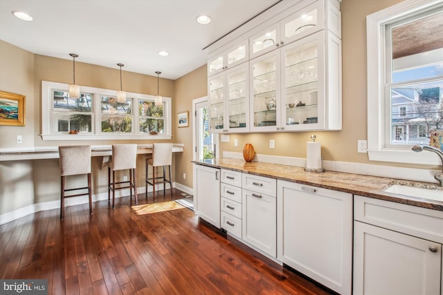 kitchen featuring glass insert cabinets, light stone counters, hanging light fixtures, white cabinetry, and a sink