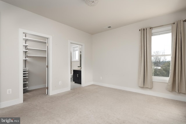 unfurnished bedroom featuring ensuite bathroom, a walk in closet, light colored carpet, and a closet