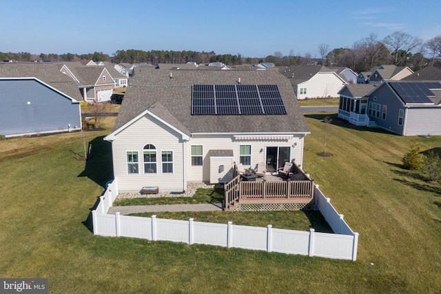 back of property featuring a wooden deck, a yard, and solar panels