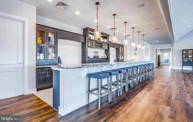 kitchen with a breakfast bar area, dark brown cabinets, dark hardwood / wood-style flooring, pendant lighting, and light stone countertops